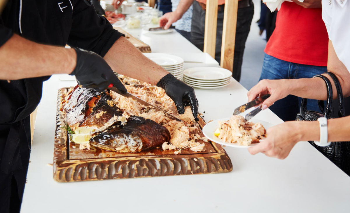 A professional chef serving grilled salmon at an event, highlighting the benefits of corporate BBQ catering.